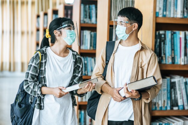 Men and women wearing masks stand and read in the library.