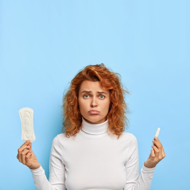 Menstrual cycle and women health concept. Dissatisfied woman holds sanitary cotton pad and tampon