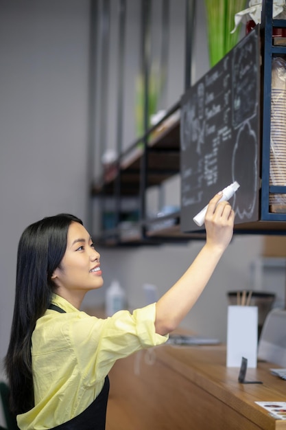 メニュー。カフェのボードにメニューを書くアジアの若い女性