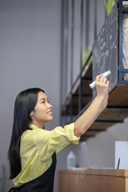 Free photo menu. asian young woman writing menu on a board in a cafe