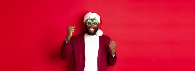 Merry christmas cheerful black man wearing funny party glasses and santa hat smiling joyful celebrat