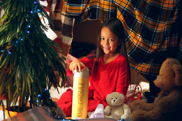 메리 크리스마스, 해피 홀리데이. 귀여운 어린 아이 소녀 실내 집에서 크리스마스 트리 근처 산타 클로스에게 편지를 씁니다. 휴일, 어린 시절, 겨울, 축하 개념