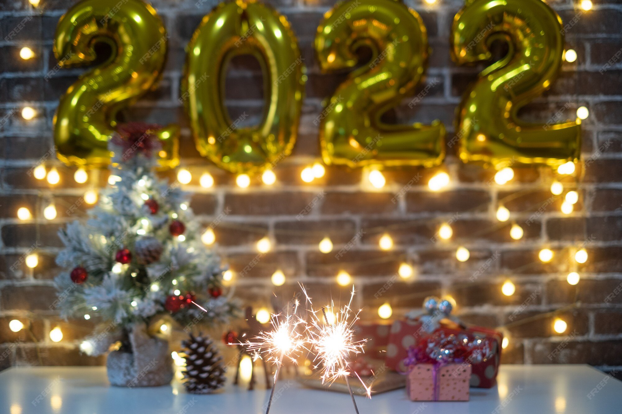 Premium Photo | Merry Christmas And Happy New Year, Defocused Small Christmas Tree On Table With Christmas Presents And 2022 In Golden Inflatable Numbers. Sparkling Lights. Brick Wall Background
