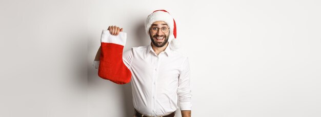 メリー クリスマスの休日の概念は、クリスマスの靴下を保持し、セルを笑顔でサンタ帽子でひげを生やした男を興奮させた