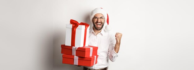 Merry christmas holidays concept excited man receiving xmas gifts and rejoicing wearing santa hat ce