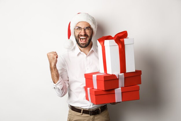 Merry christmas, holidays concept. Excited man receiving xmas gifts and rejoicing, wearing santa hat, celebrating New Year 