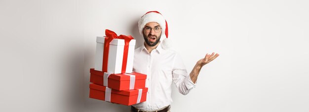 Merry christmas holidays concept man looking confused while holding xmas gifts shrugging puzzled sta
