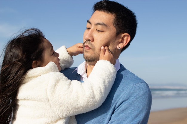 自由快乐的父亲和女儿照片在海滩上花费时间。日本家庭做鬼脸,拥抱、欢笑,在鬼混。休闲、家庭时间、教育的概念