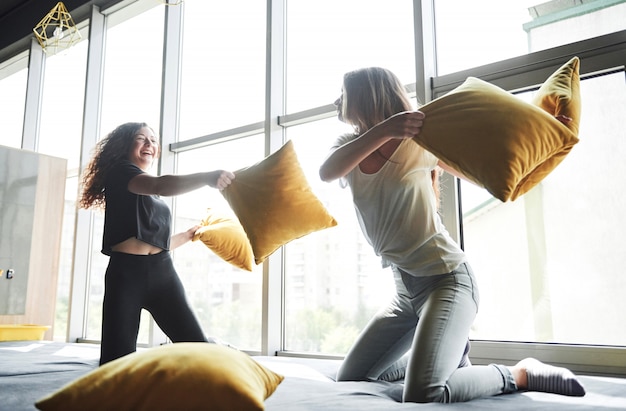 Free photo merry happy girlfriends are fighting with pillows.