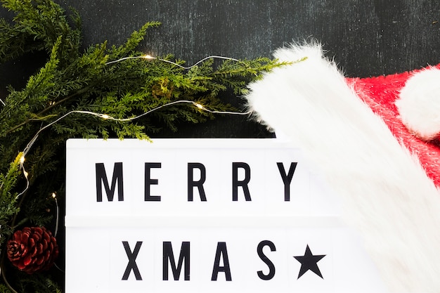Бесплатное фото Веселая рождественская надпись на борту с шляпой и ветками санта