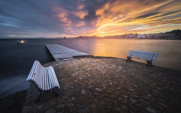 風光明媚な夕日の前景に木製の桟橋とベンチがある魅惑的な海の景色