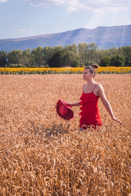 밀밭 앞에서 포즈를 취하는 빨간 드레스를 입은 매력적인 여성의 매혹적인 샷