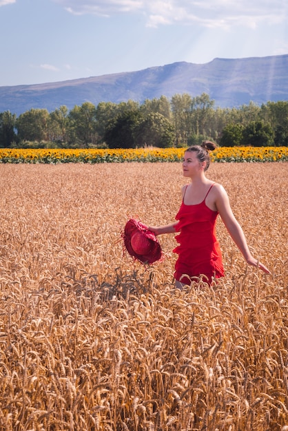 Mesmerizing shot of an attractive female in a red dress posing at front in a wheat field