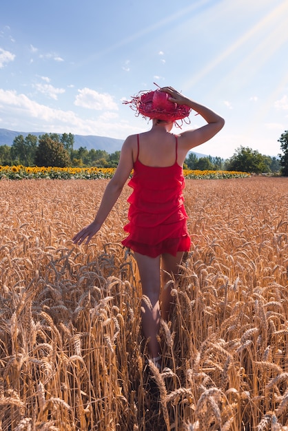 Mesmerizing shot of an attractive female in a red dress posing in a wheat field