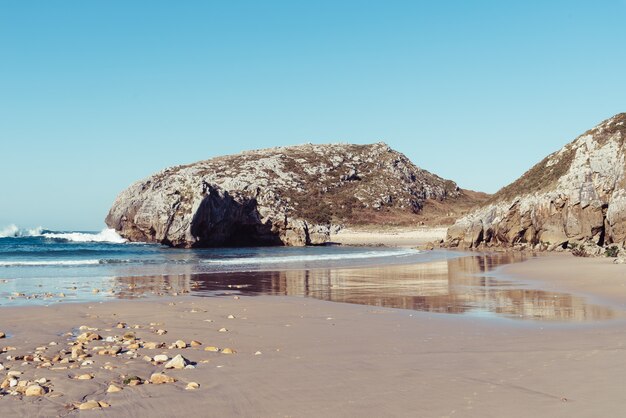 Mesmerizing view of the waves crashing on the rocks near the shore on a clear day