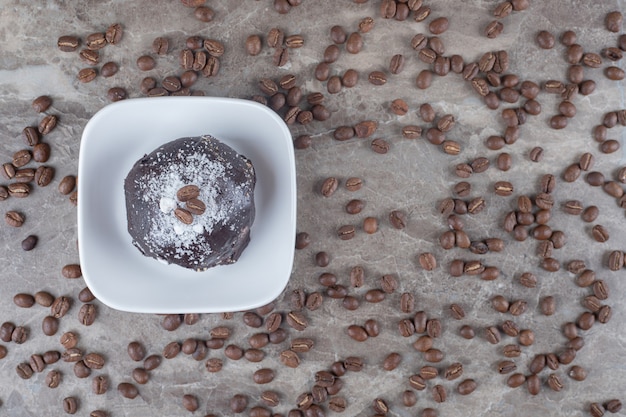 Pasticcio di chicchi di caffè intorno a un piccolo piatto con una torta ricoperta di cioccolato su una superficie di marmo