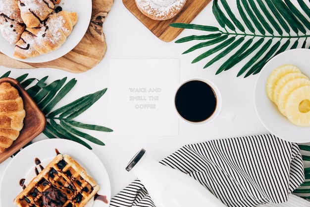 Message on notepad surrounded with baked breakfast; coffee and pineapple slices on white desk