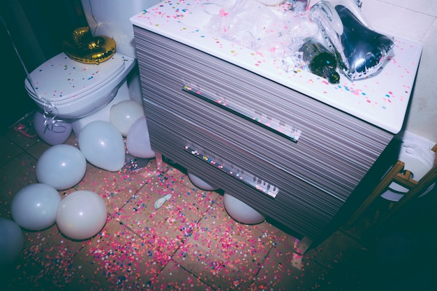 Бесплатное фото Грязная ванная комната с пустой бутылкой; разноцветные конфетти и белые шарики после дня рождения