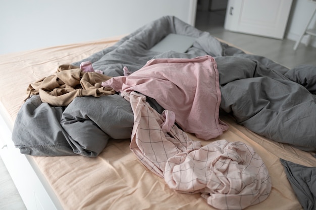 Грязная спальня с одеждой на кровати под высоким углом
