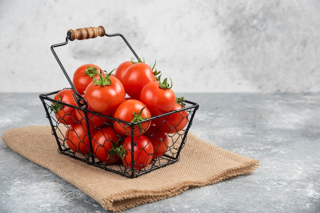 Metal basket of fresh organic tomatoes on marble.