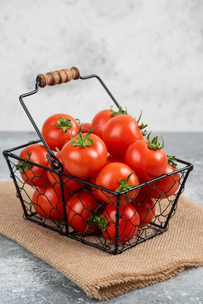 Metal basket of fresh organic tomatoes on marble.