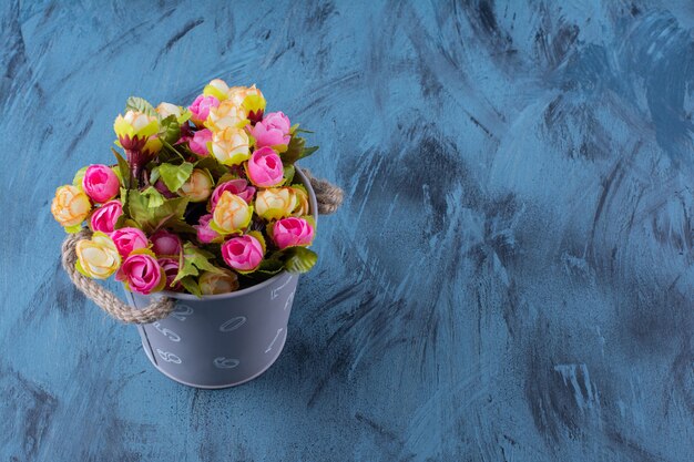 Metal bucket of colorful flower arrangement on blue.