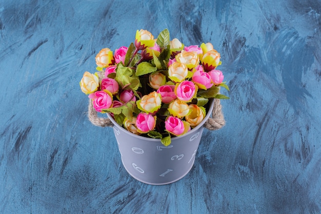 Metal bucket of colorful flower arrangement on blue.