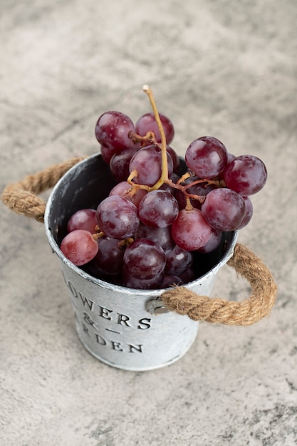 Metal bucket of juicy red grapes on stone background. 