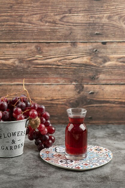 Metal bucket of red fresh grapes and glass of juice on marble table. 