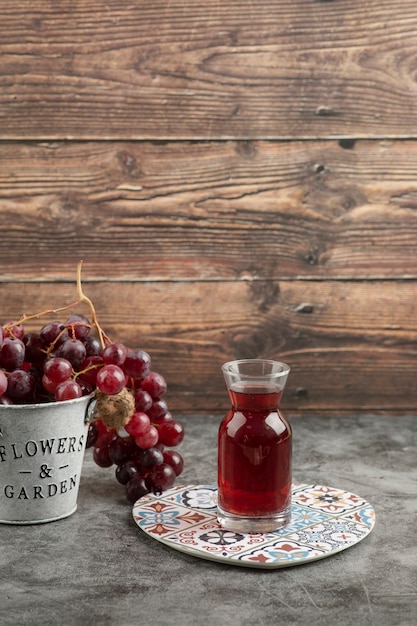 Metal bucket of red fresh grapes and glass of juice on marble table.