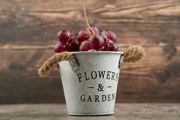 Metal bucket of red fresh grapes on marble table. 