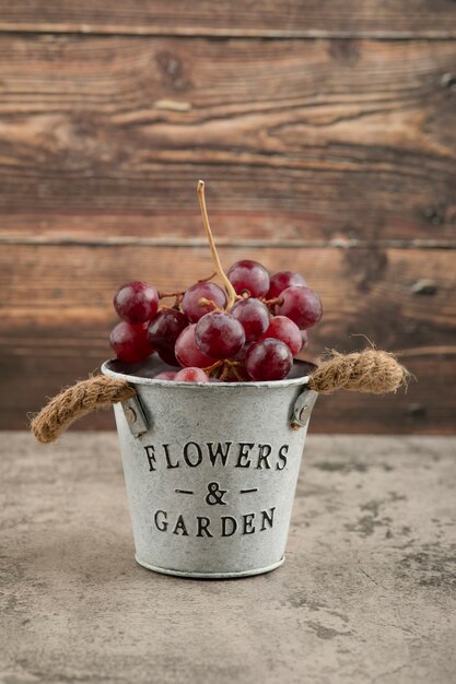 Metal bucket of red fresh grapes on marble table. 