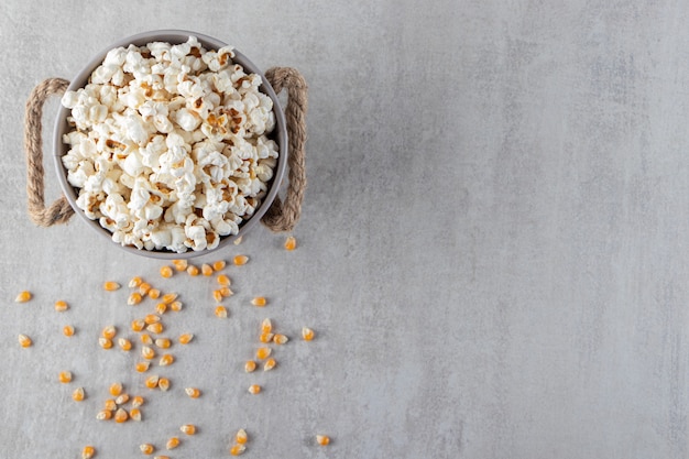 Metal bucket of salted popcorn placed on stone background. 