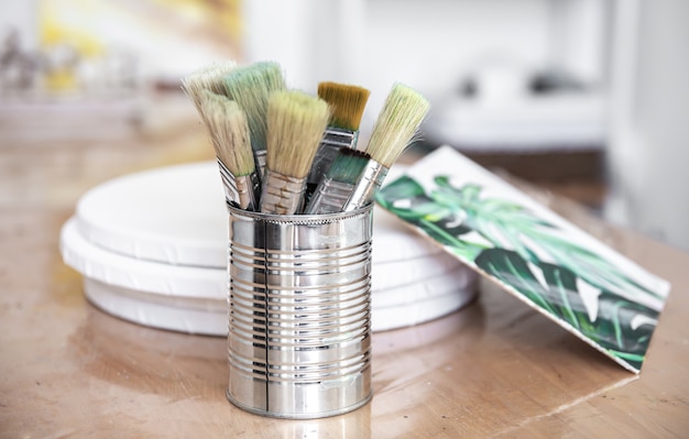 A metal can with paint brushes and a canvas with a picture of a monstera