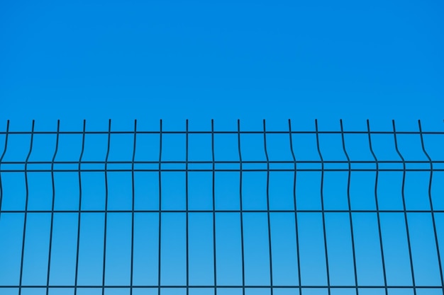Metal fence against the background of a blue boundless sky a blurred background the idea of freedom and the removal of restrictions a background for a poster or postcard