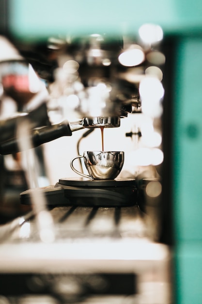 金属製の大型コーヒーメーカーマシンが金属製のカップにコーヒーを注ぐ