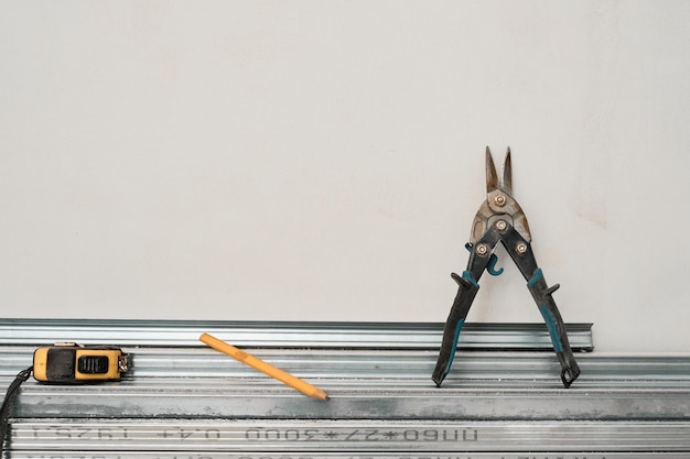 Free photo metal profiles for drywall, laid on the floor against the wall, tape measure and metal scissors. preparing profiles for the installation of a wall or ceiling frame