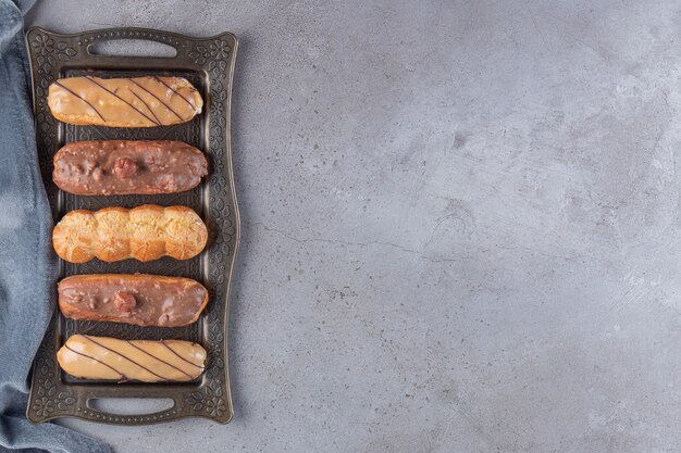 Metal tray of sweet tasty eclairs on stone table. 