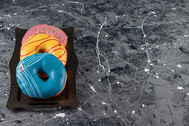 Metal tray of various delicious donuts with sprinkles on marble surface