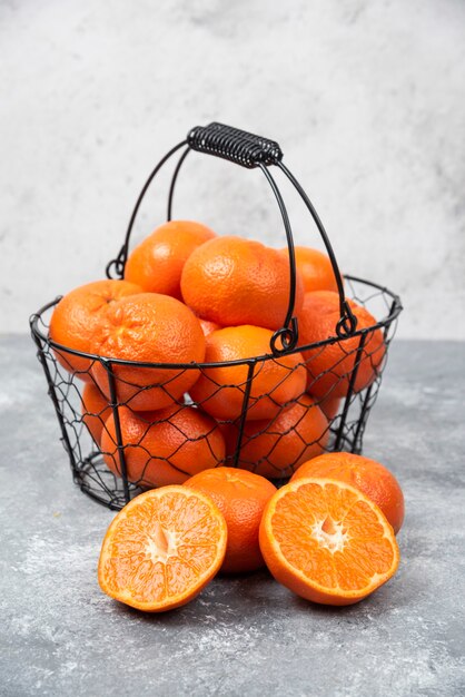 A metallic black basket full of juicy orange fruit on stone table .