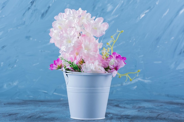 Free photo a metallic bucket full of beautiful colorful flowers on blue.