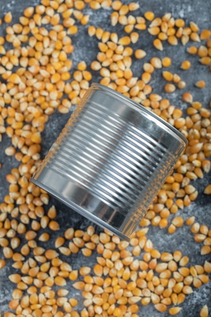 Metallic can with uncooked popcorns on marble.