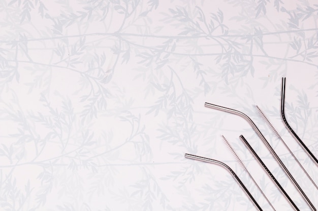 Metallic straws on background with leaves