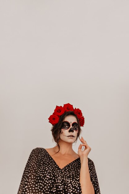 Mexican girl with roses in wavy hair mysteriously  in white room.