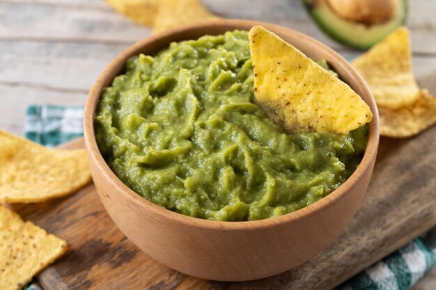 Mexican guacamole with nacho chip in wooden bowl on rustic wooden table Top view Traditional mexican food