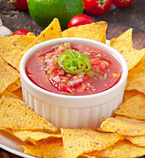 Mexican nacho chips and salsa dip in bowl on wooden