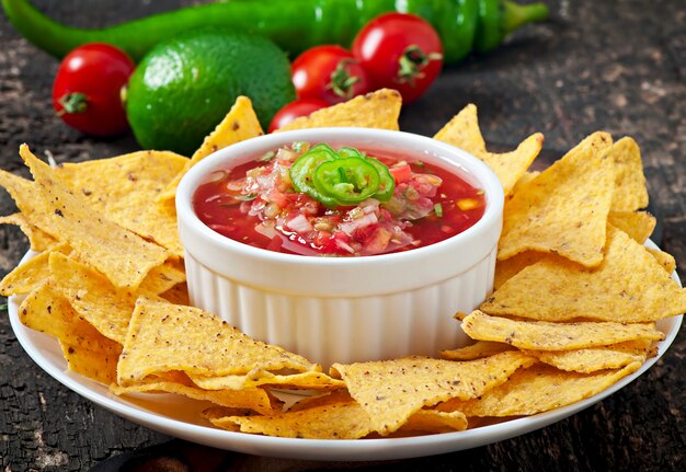 Mexican nacho chips and salsa dip in bowl on wooden