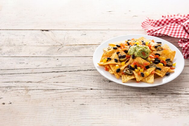 Mexican nachos tortilla chips with black beans, guacamole, tomato and jalapeno on wooden table