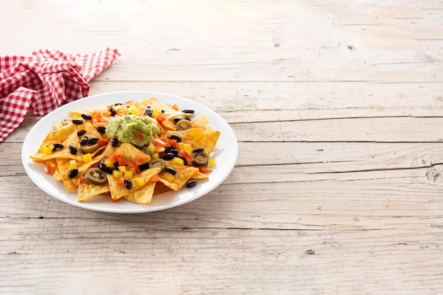 Mexican nachos tortilla chips with black beans, guacamole, tomato and jalapeno on wooden table