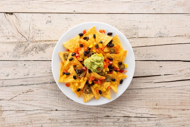 Mexican nachos tortilla chips with black beans, guacamole, tomato and jalapeno on wooden table